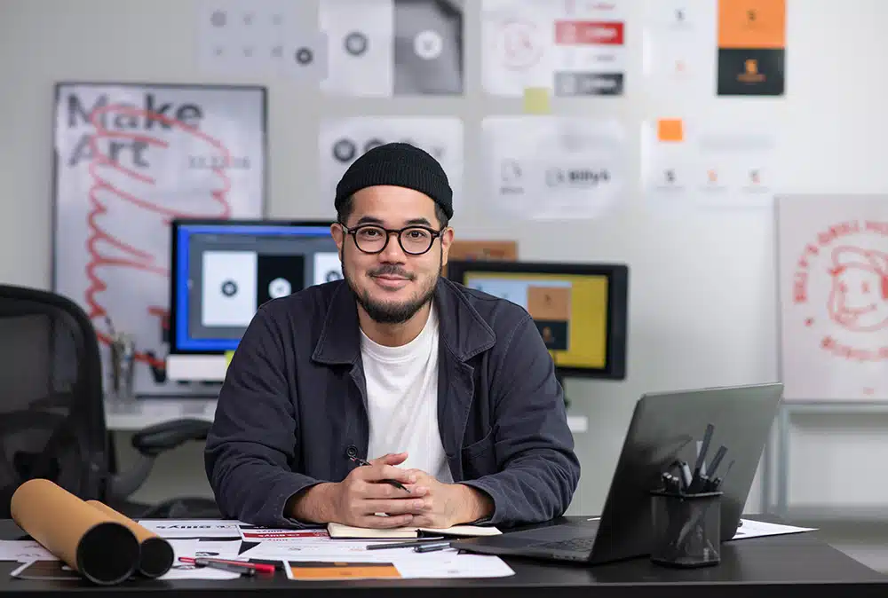 Technical web worker in an office, smiling as he leans across his desk